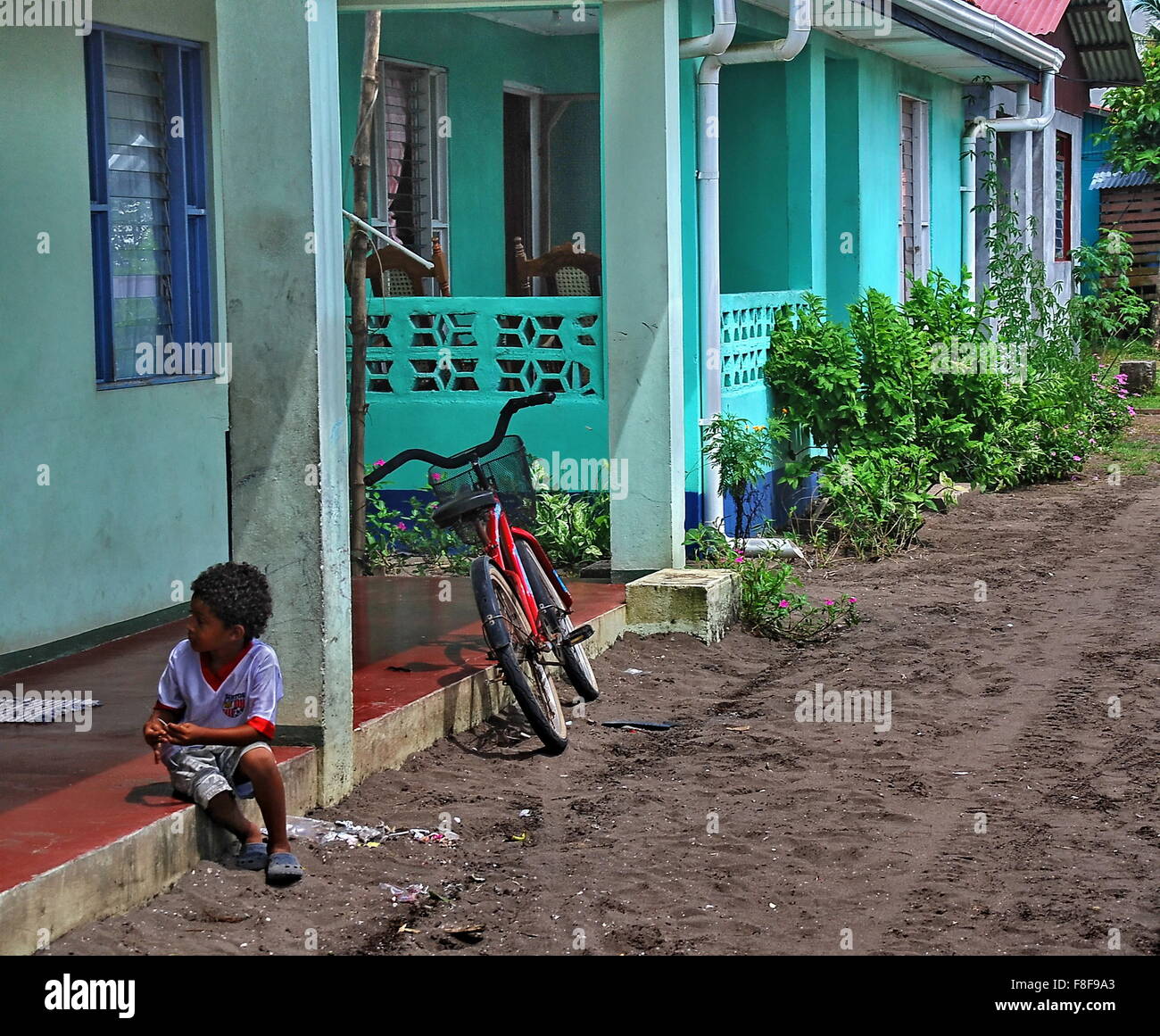 Small boy and bicycle sitting at his colorful aqua colored home and dirt road in the small town of Tortugurero, Costa Rica. Stock Photo