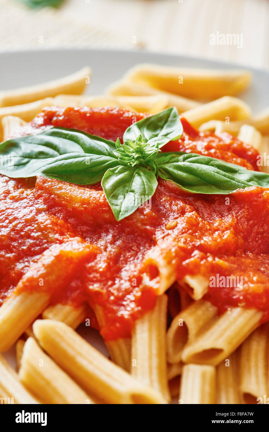 Wheat pasta with tomato sauce on white plate surrounded by basil and tomato on wooden table Stock Photo