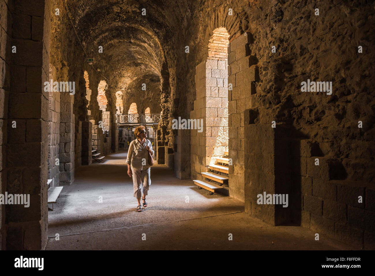 Woman travel solo, view of a middle aged female tourist in Catania exploring the subterranean corridor beneath the ancient roman amphitheatre, Sicily. Stock Photo