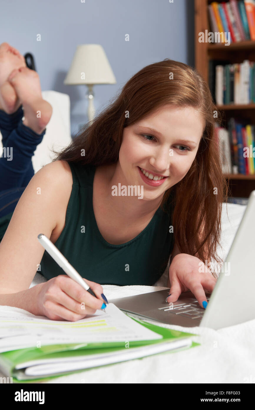 Teenage Girl Using Laptop To Do Homework In Bedroom Stock Photo