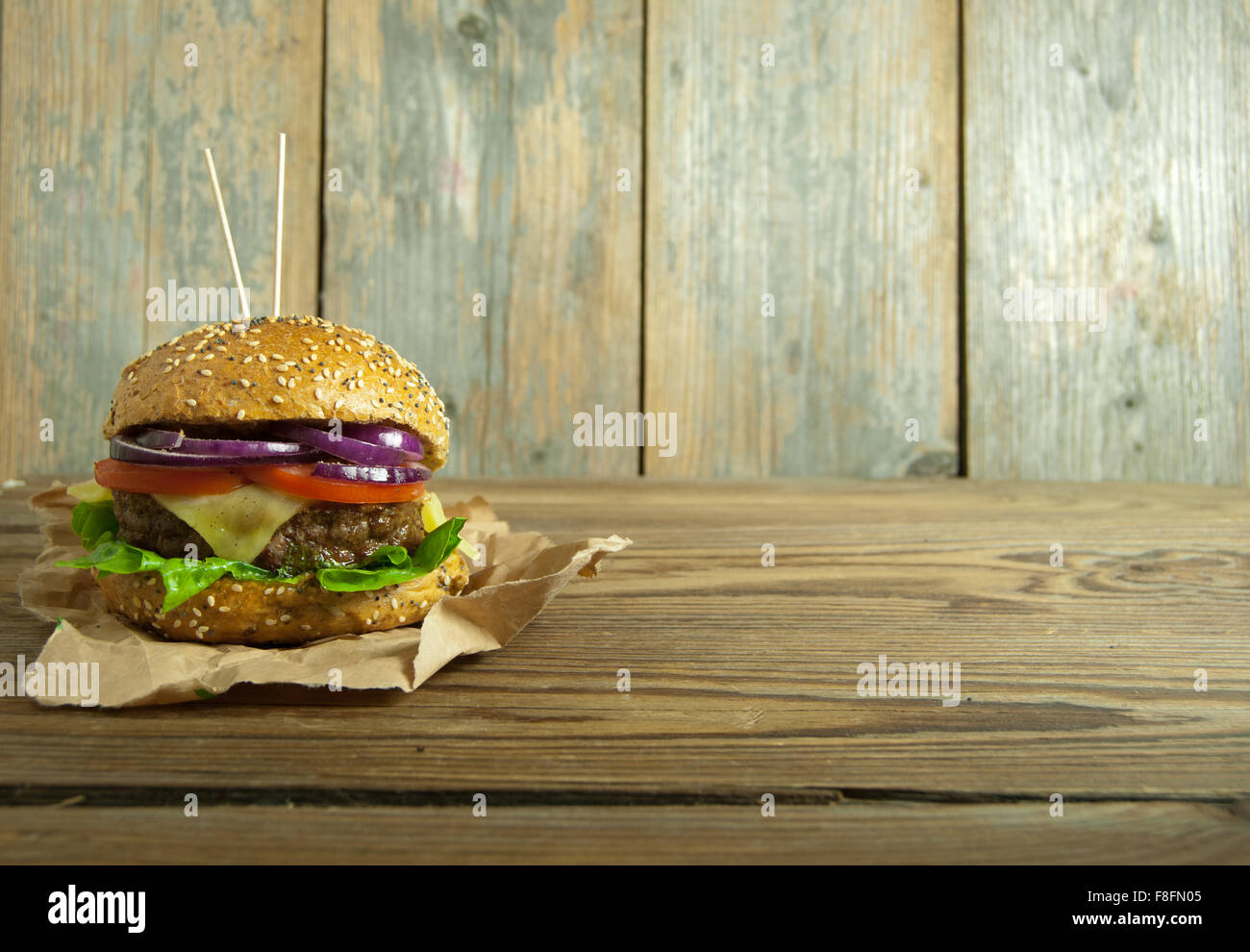 Gourmet burger with melted cheese, tomato and onion filling on top of a wooden chopping board with space for text Stock Photo