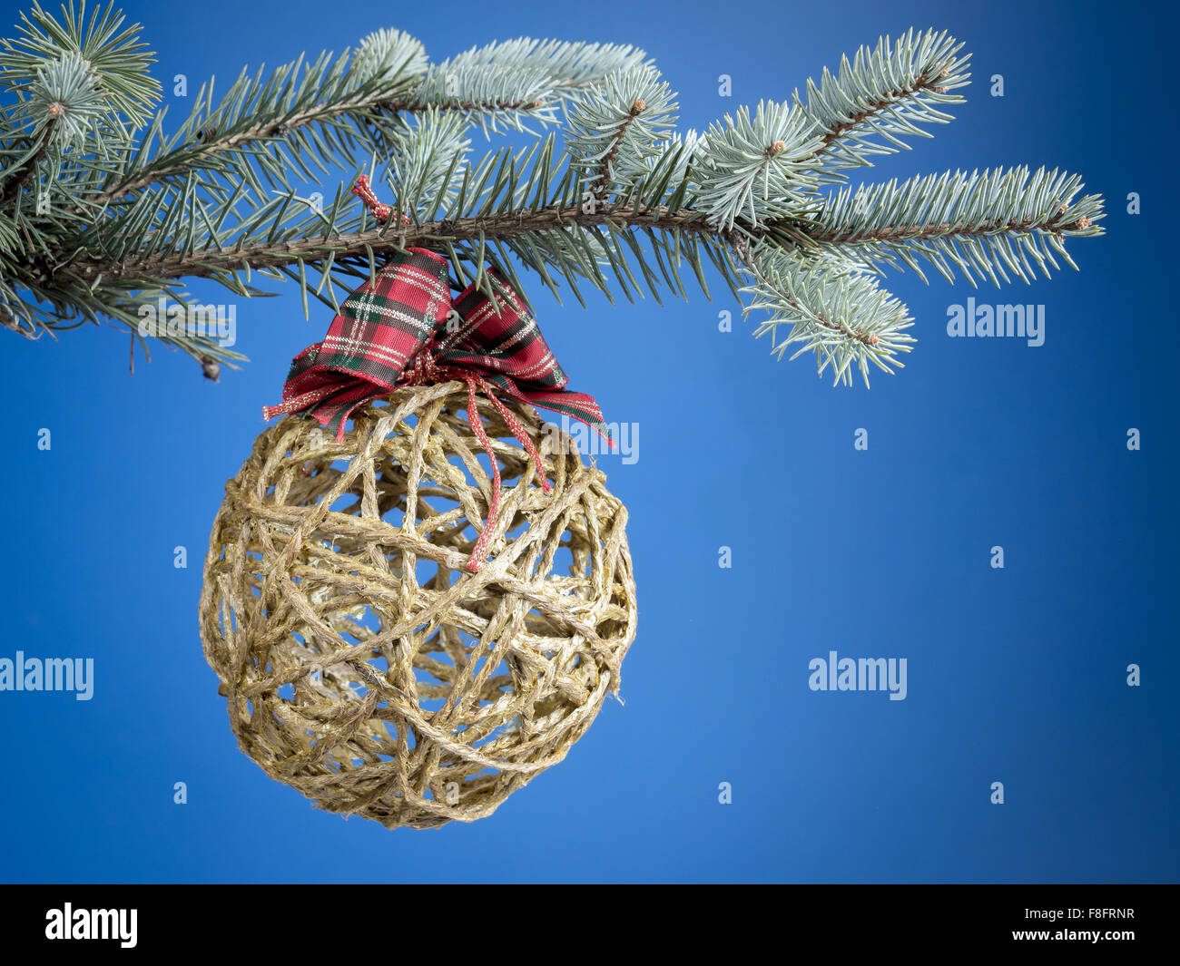 Christmas ball formed from hemp string hanging on spruce branch over blue background Stock Photo