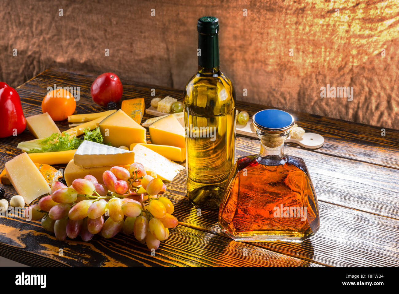 Appetizers at a party with a large assortment of speciality cheeses, fresh grapes, bottle of wine and whiskey decanter on a wooden table. Stock Photo