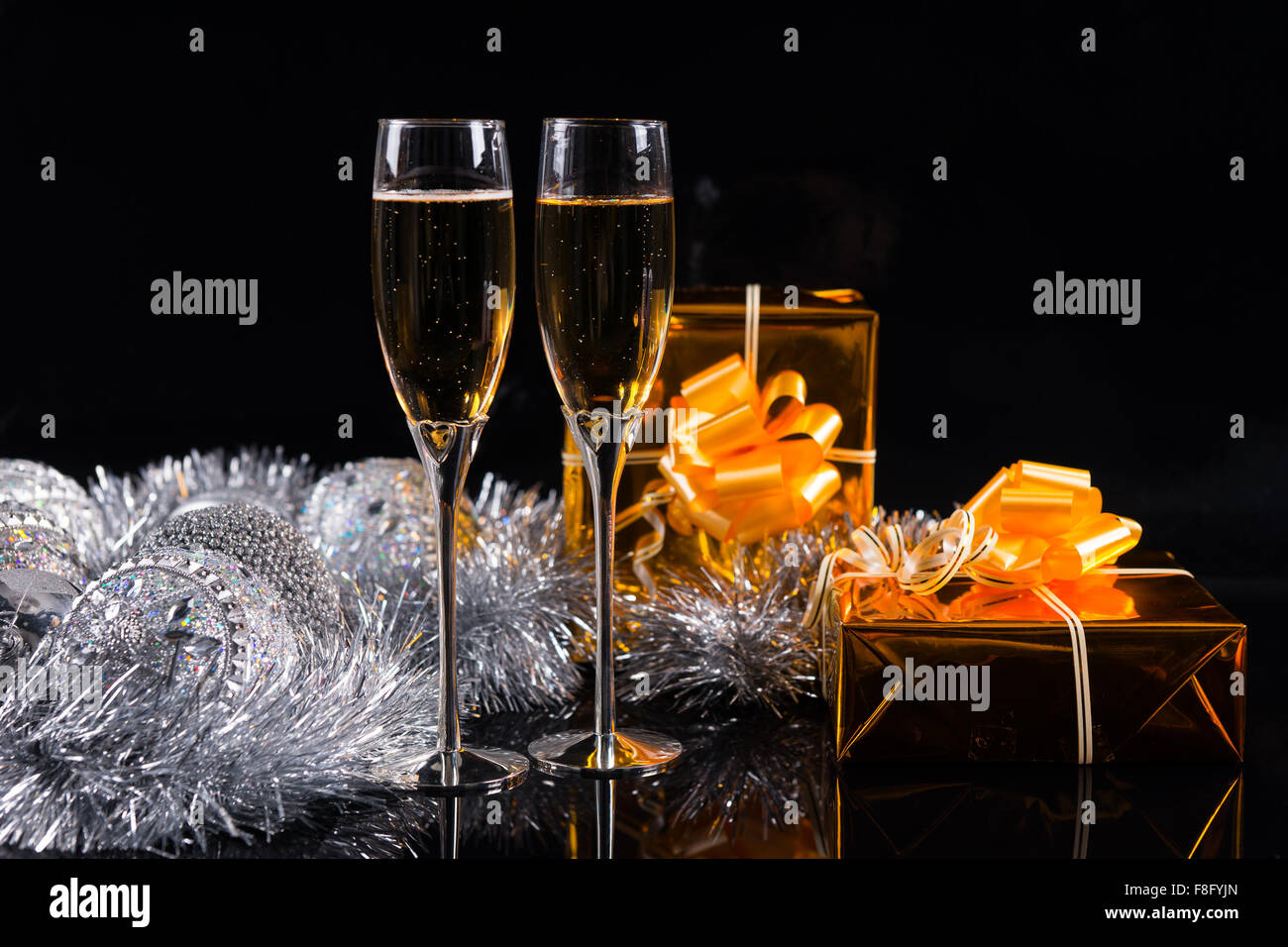 Two stemmed glasses full of champagne, Christmas silver tinsel and two gift boxes wrapped in golden shiny paper on a table with Stock Photo
