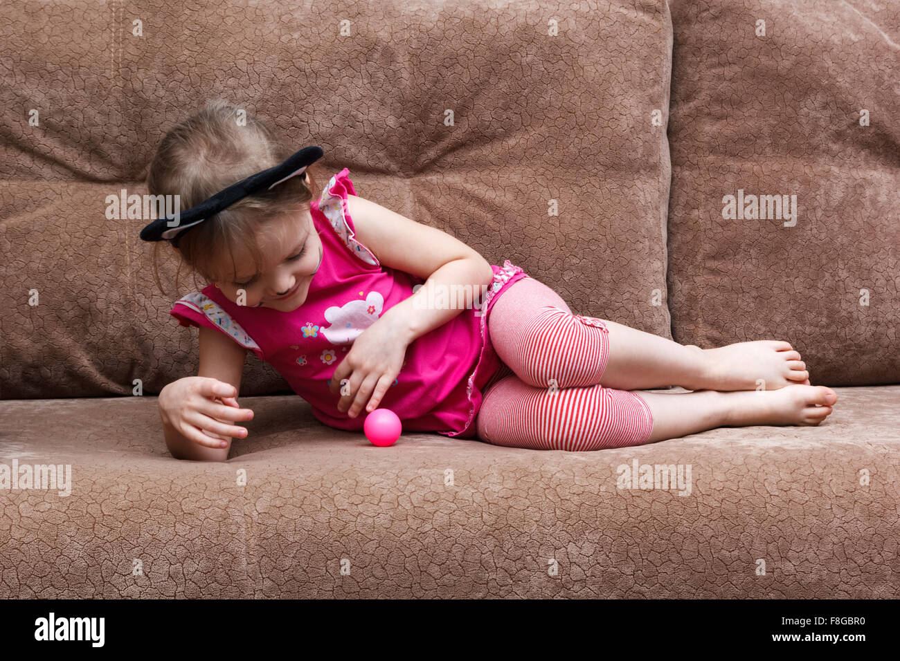 little girl with cat face painting play ball on a couch Stock Photo