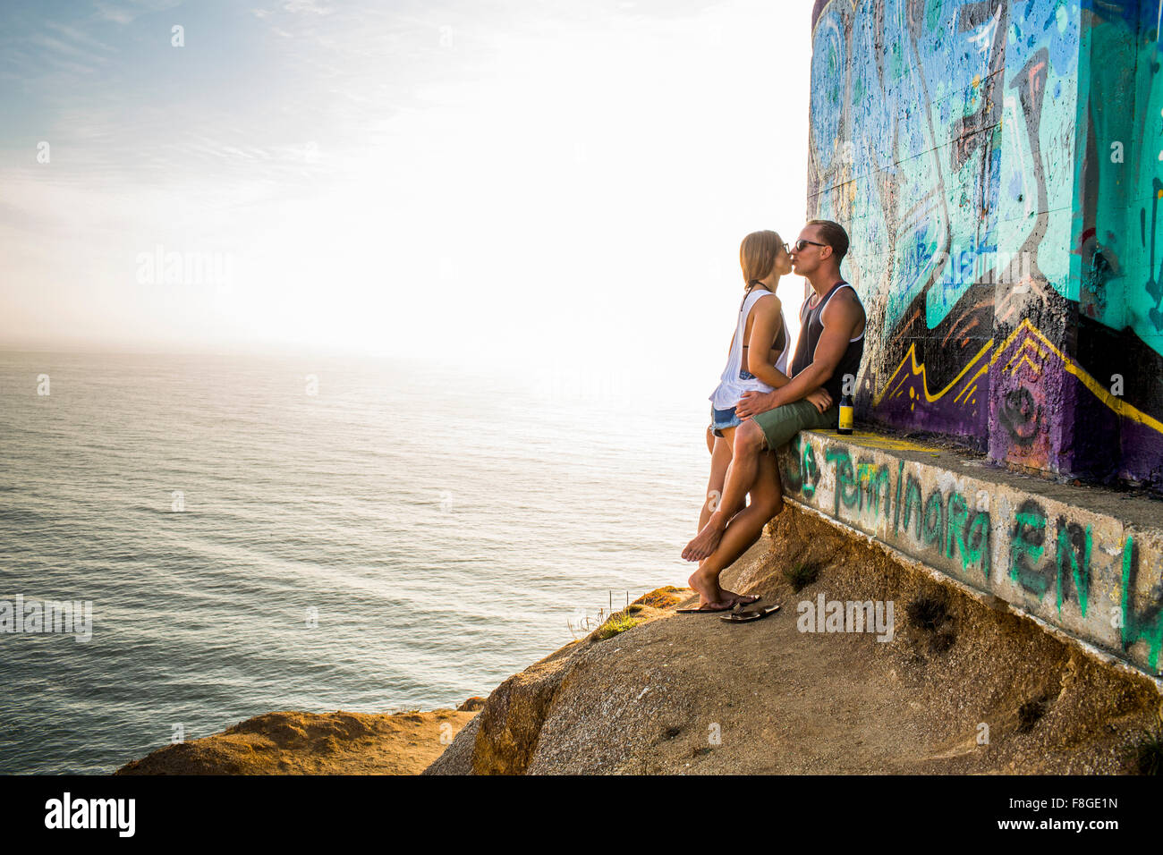 Caucasian couple kissing at mural on cliff Stock Photo