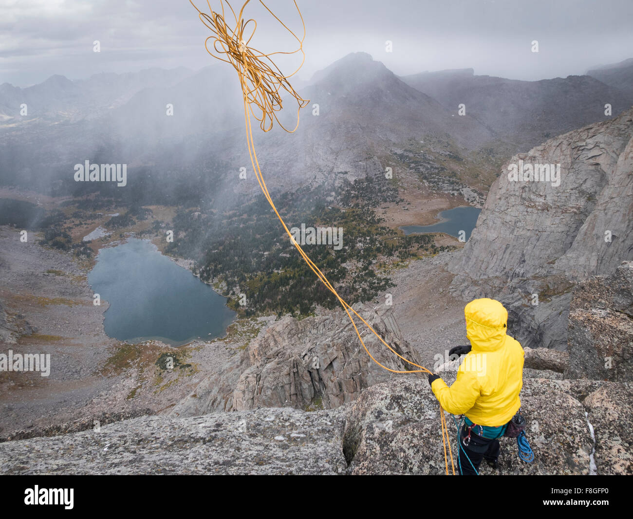 Caucasian climber throwing rope down mountainside Stock Photo