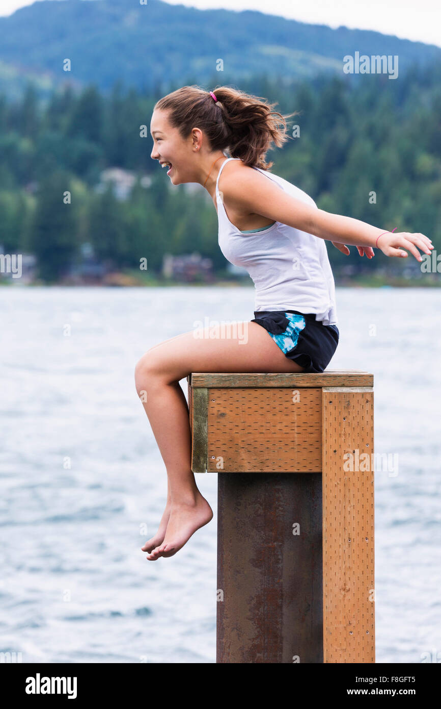 Mixed race girl sitting on wooden pedestal at lake Stock Photo