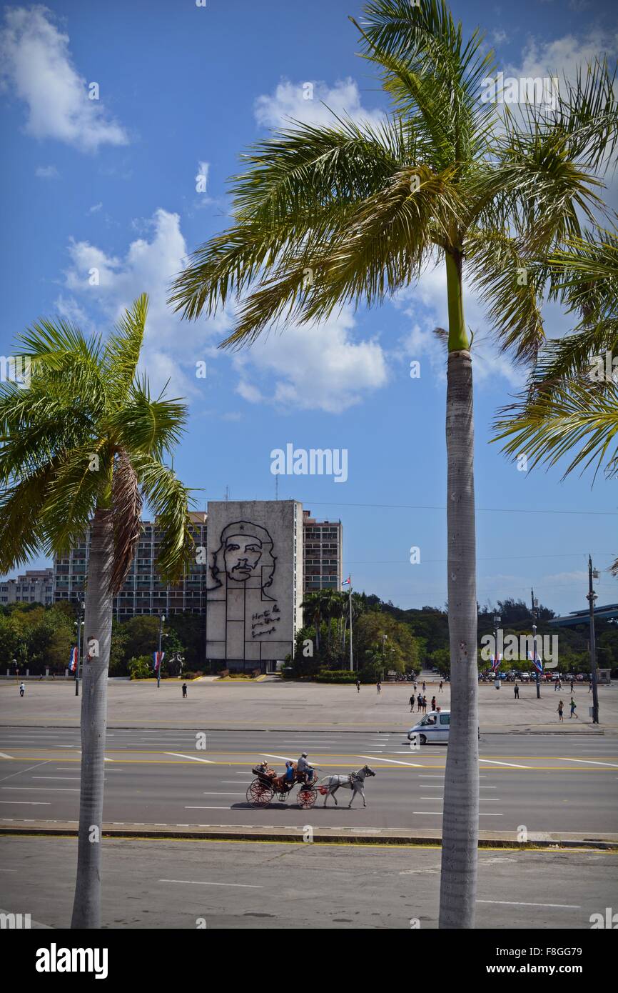 horse and carriage driving across Revolution Square in view of the block with the iconic image of Che Guevara with palm trees Stock Photo