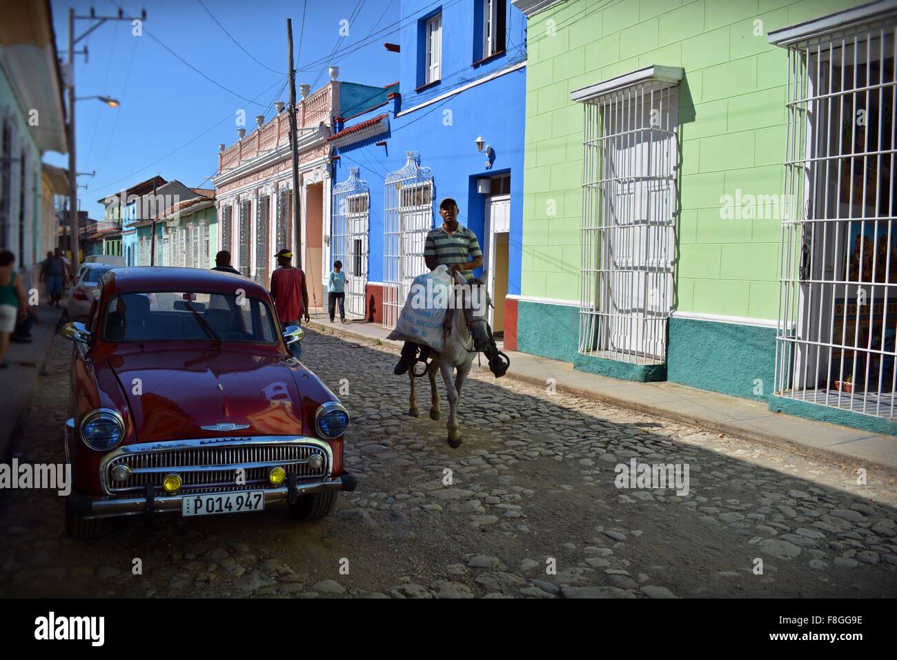 horseman and pedestrians walking on a partially shaded cobbled street in colorful Trinidad Sancti Spiritus Province Cuba Stock Photo