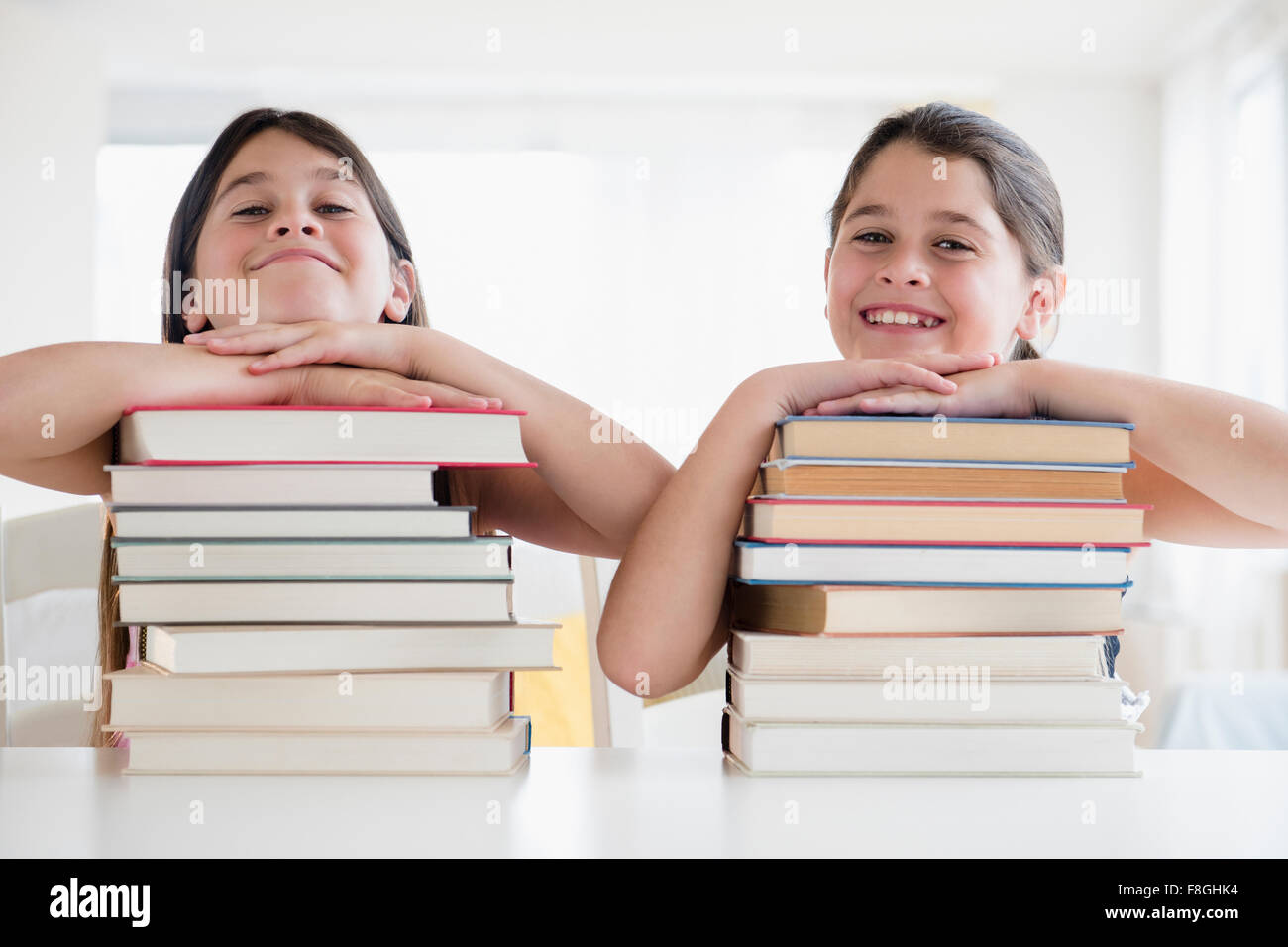 Caucasian twin sisters resting on stacks of books Stock Photo