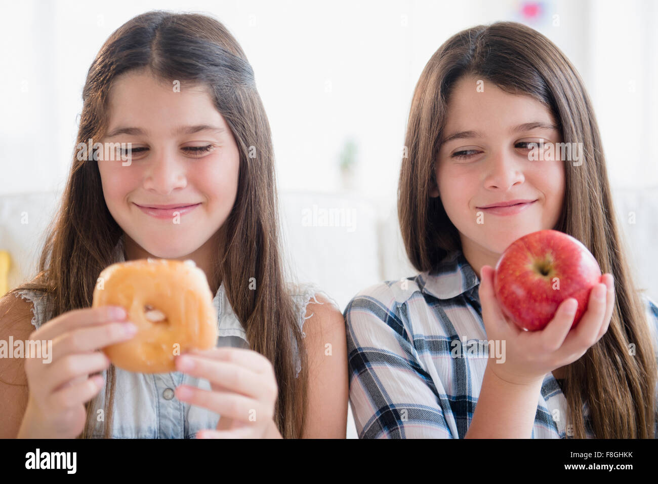 Caucasian twin sisters eating healthy and unhealthy snacks Stock Photo