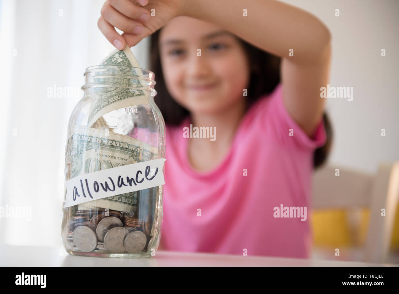 Girl saving allowance in money jar Stock Photo