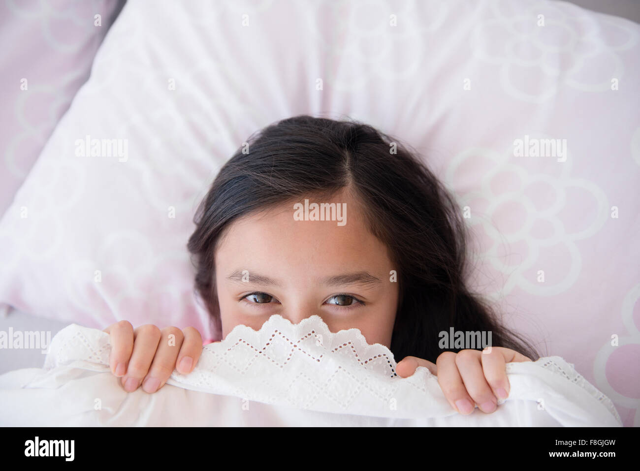 Girl peeking out from bed blankets Stock Photo