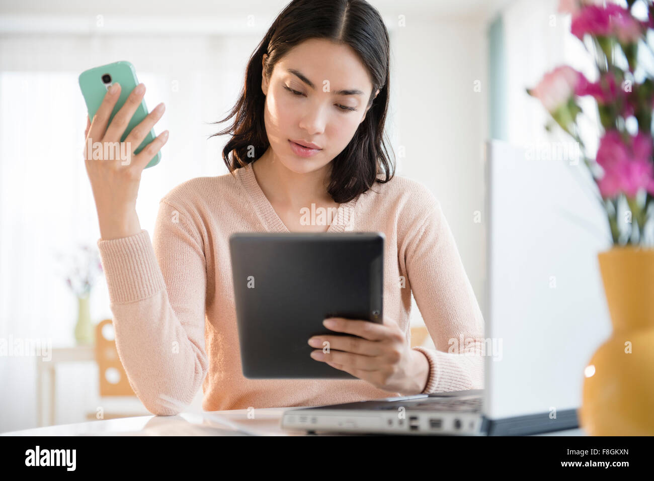 Hispanic woman using cell phone and digital tablet Stock Photo