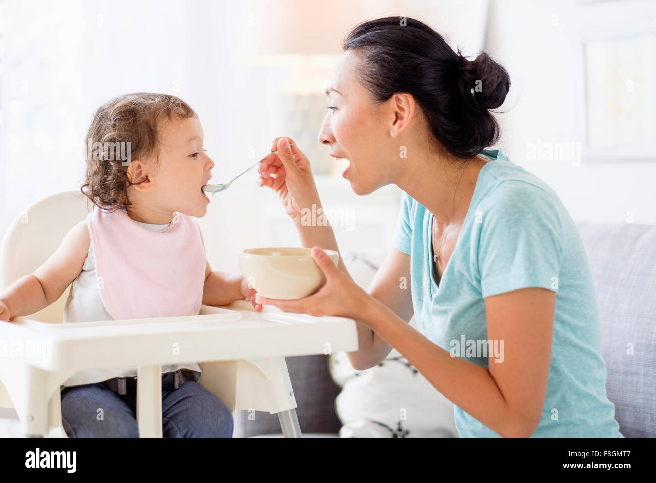 Mother feeding baby daughter in high chair Stock Photo