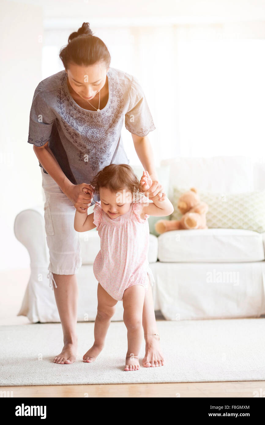 Mother helping baby daughter walk in living room Stock Photo
