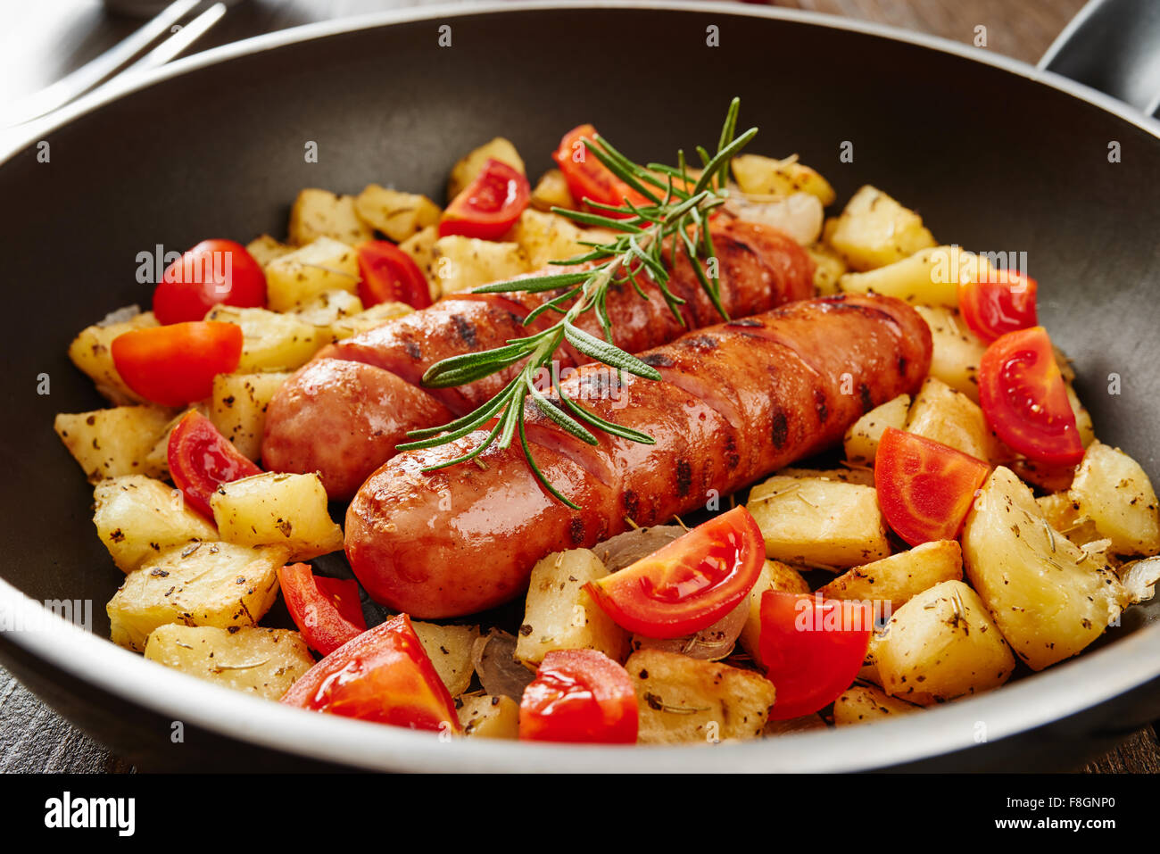 Grilled sausage in pan on wooden table surrounded by ingredients Stock Photo