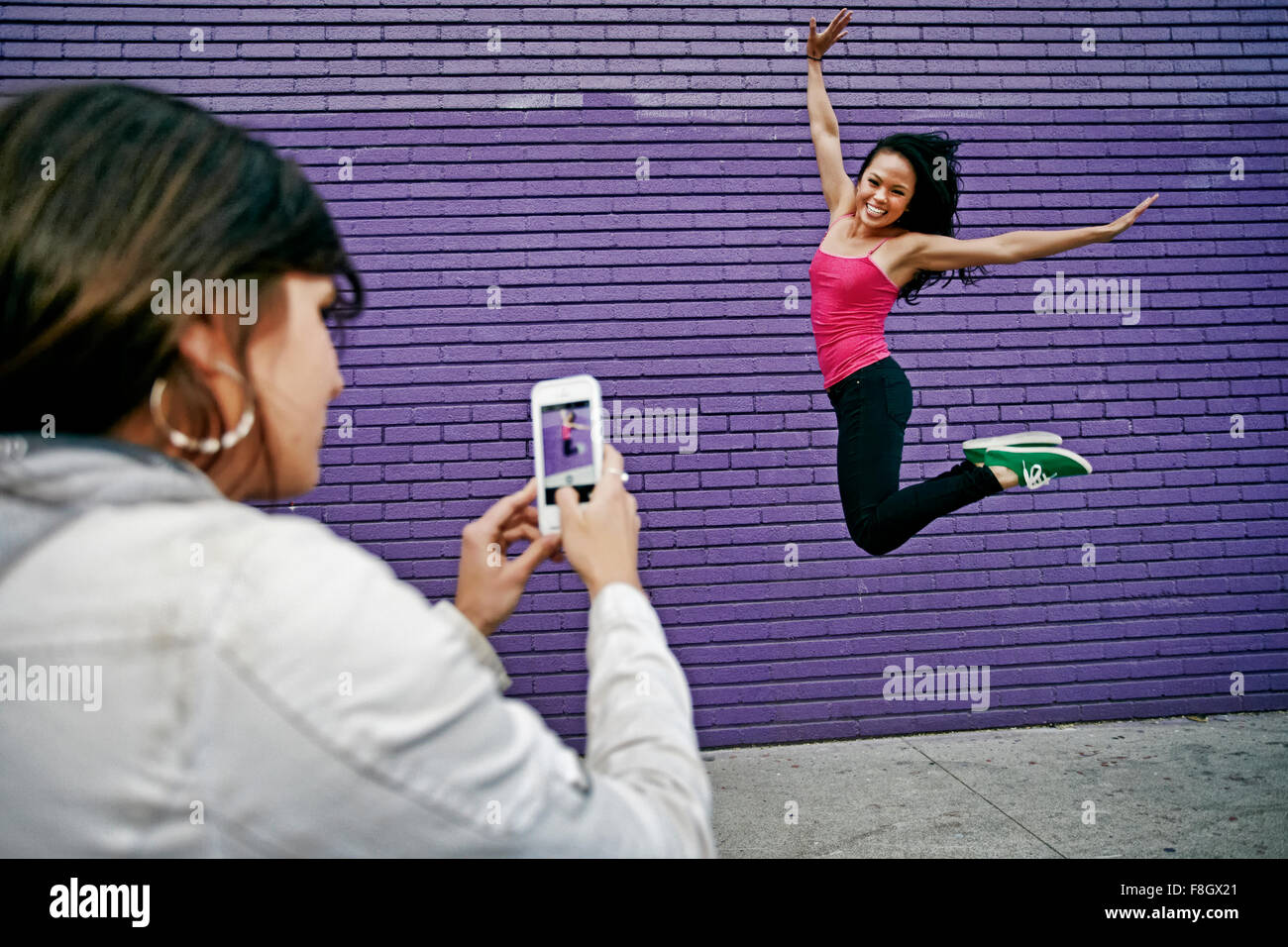 Woman photographing friend jumping for joy Stock Photo