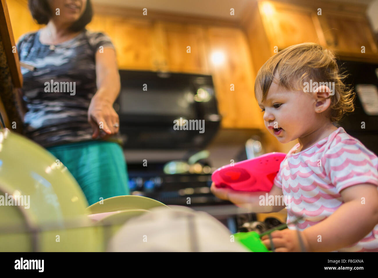 Baby girl helping mother load dishwasher Stock Photo