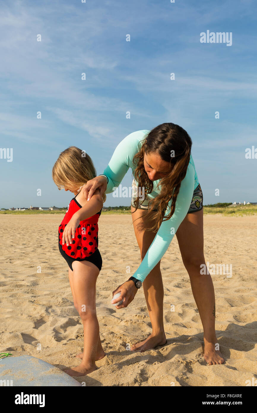 Mother spraying sunscreen on daughter at beach Stock Photo