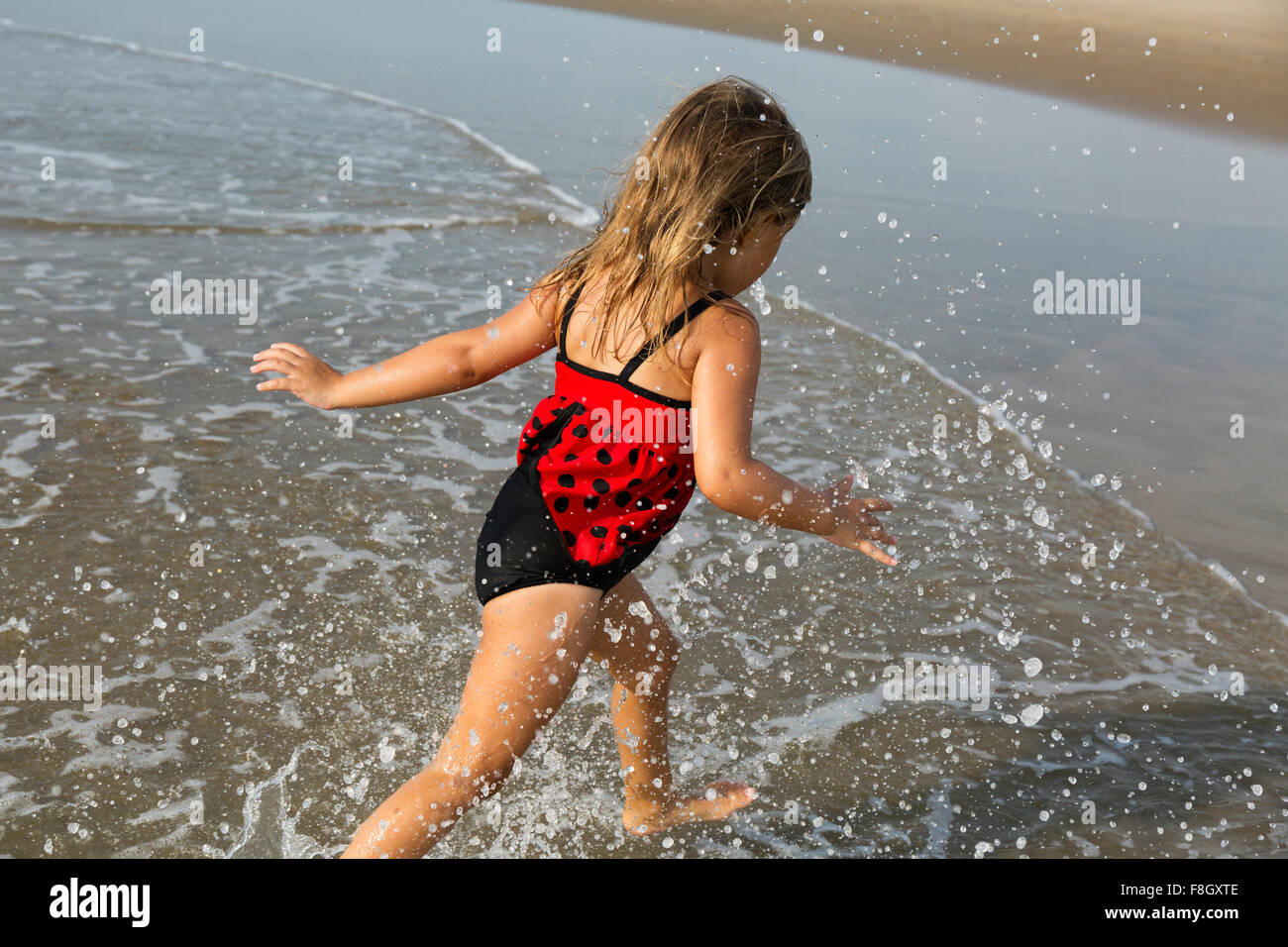 Mixed race girl splashing in waves on beach Stock Photo