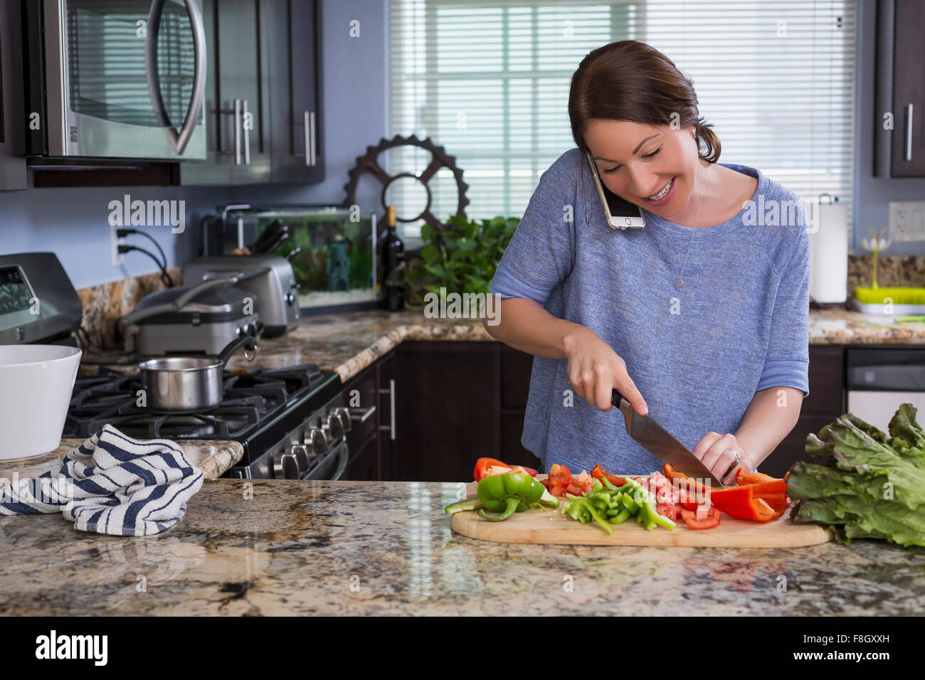 Mixed race woman talking on phone and chopping vegetables Stock Photo