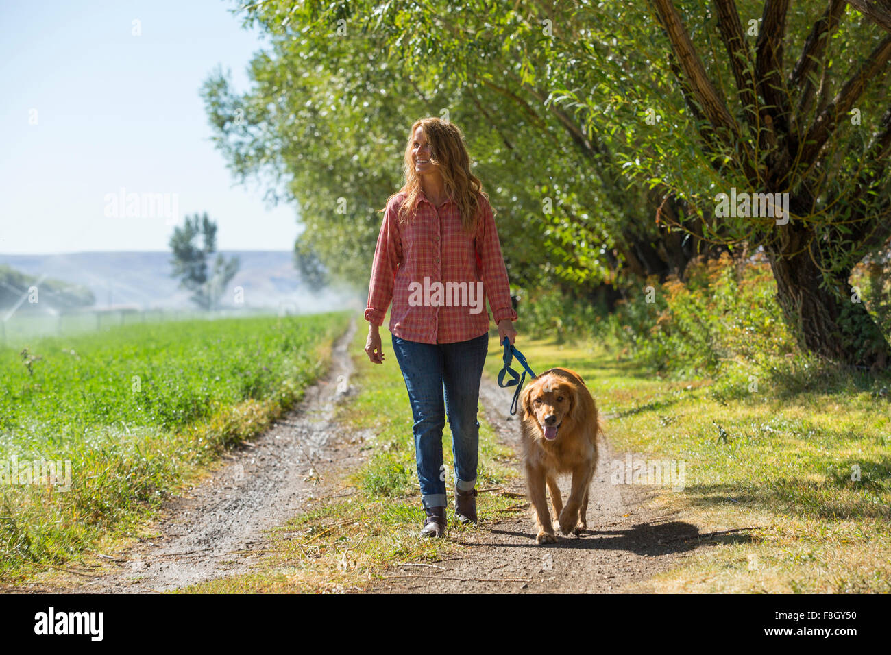 Caucasian woman walking dog on dirt path Stock Photo