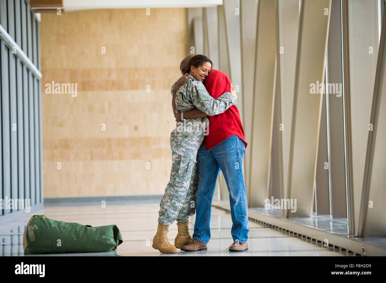 African American soldier hugging husband in airport Stock Photo