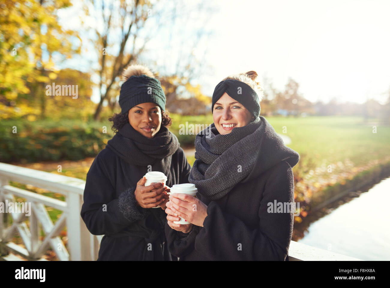 Two young women standing on bridge and holding coffee to go, smiling Stock Photo