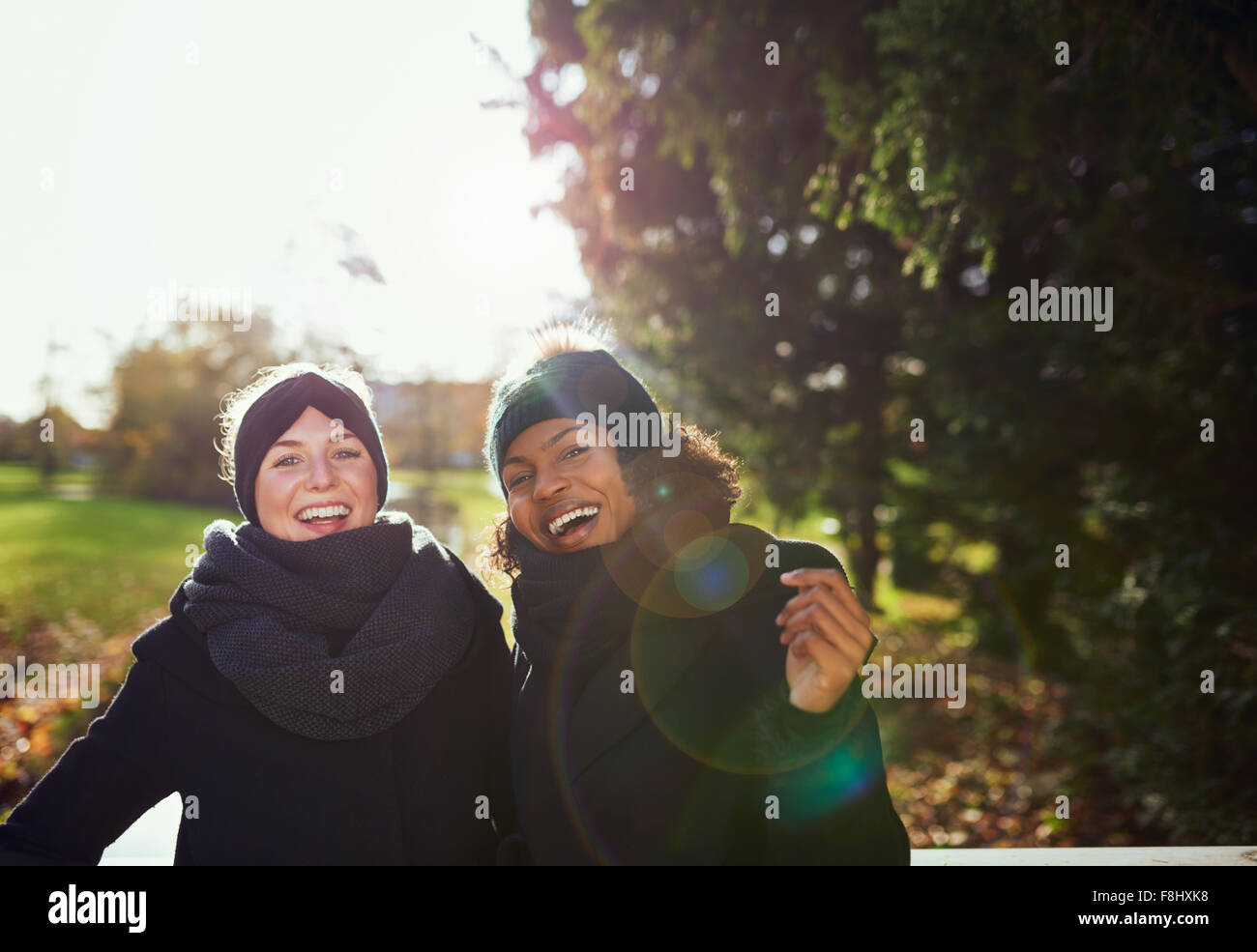 Two smiling women standing on bridge in park.Sunny Stock Photo