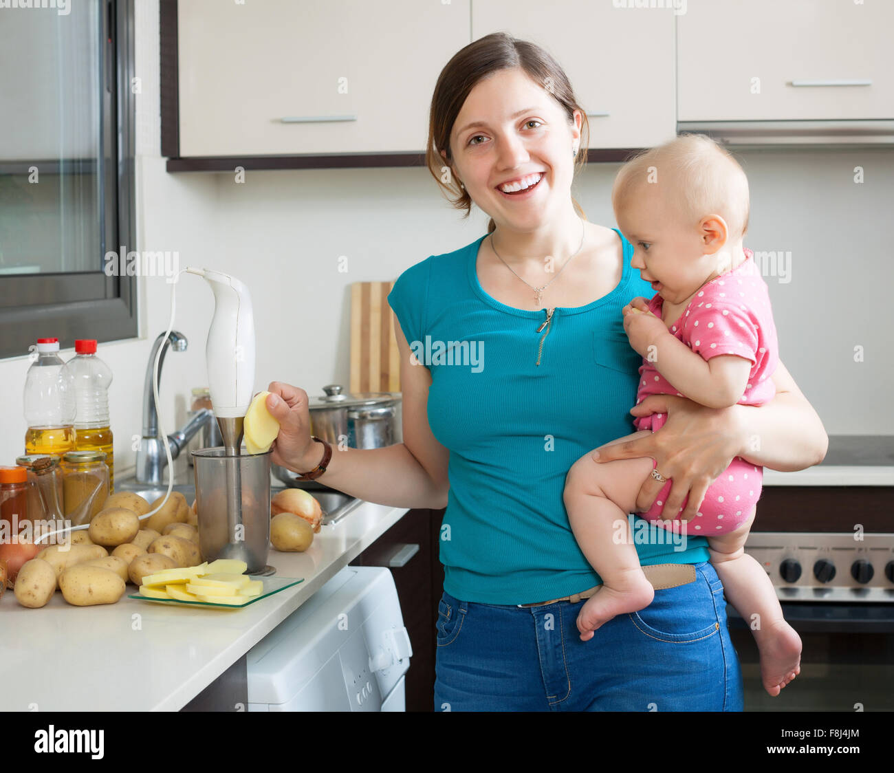 Happy woman with child together cooking mashed potatoes in kitchen at home Stock Photo