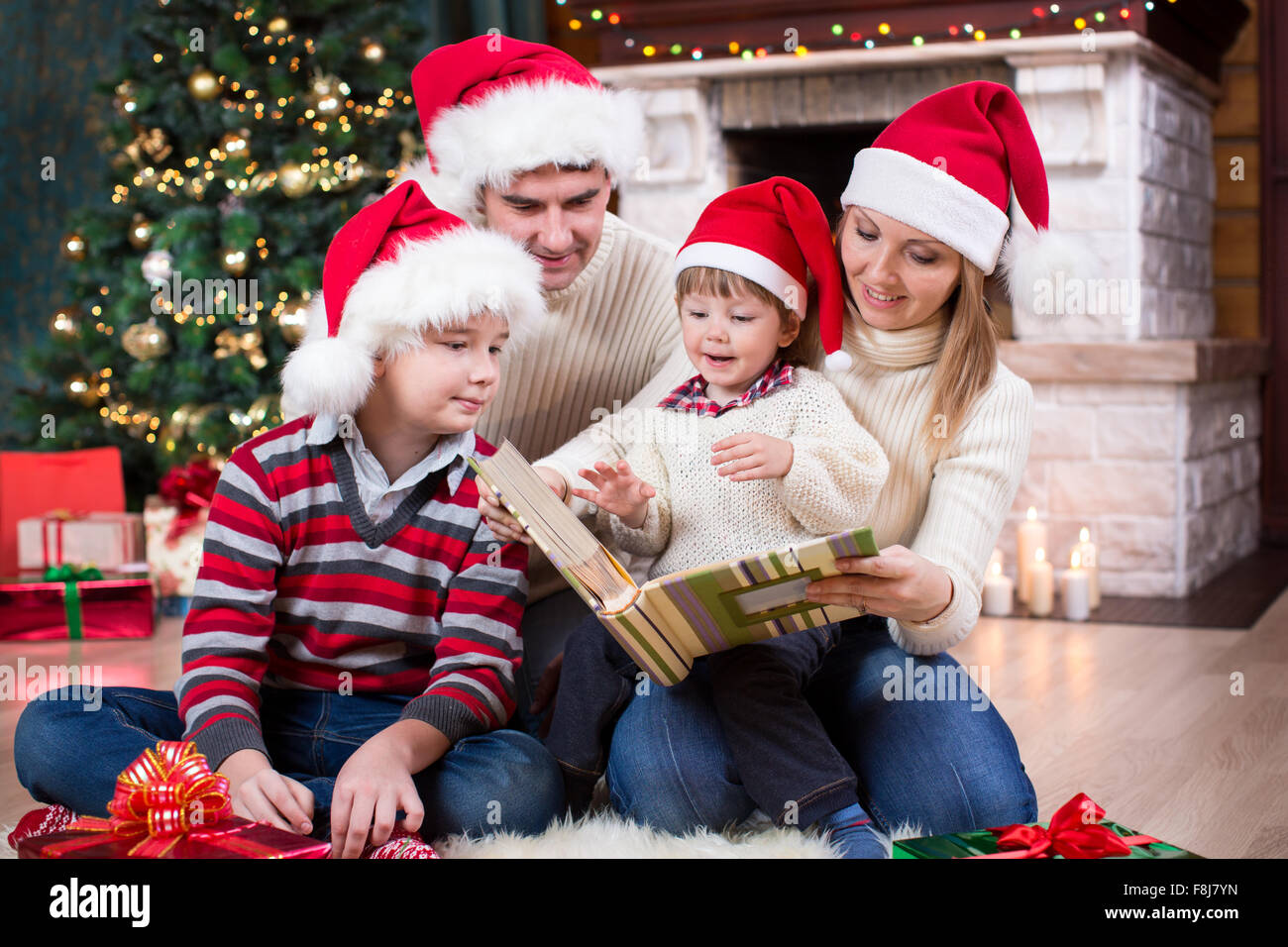 Family reviewing their photos in album near Christmas tree in front of fireplace Stock Photo