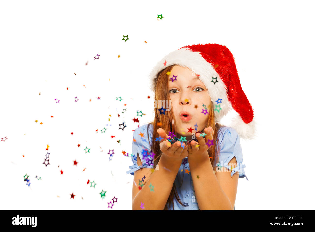 Girl blows confetti from palms in Santa hat Stock Photo