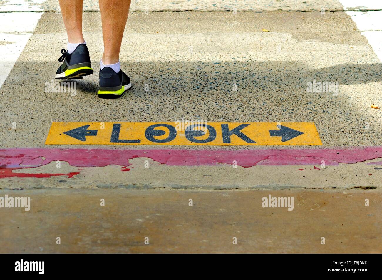A black and yellow plastered look both ways sign on the road, with eyes drawn inside the o, which warns pedestrians to be carefu Stock Photo