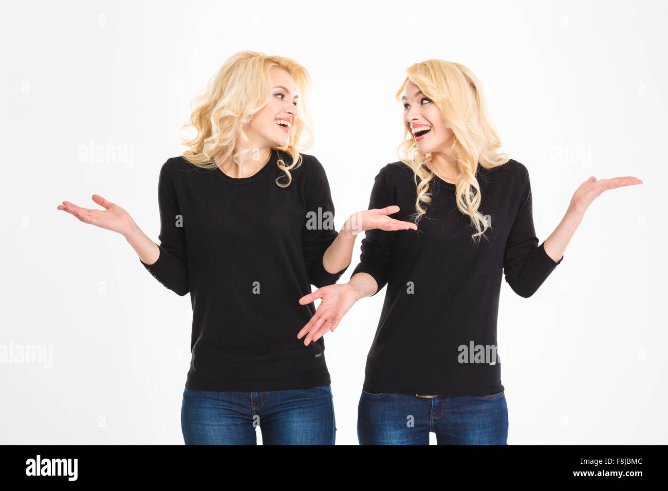 Portrait of a laughing sisters twins looking at each other and shrugging shoulders isolated on a white background Stock Photo