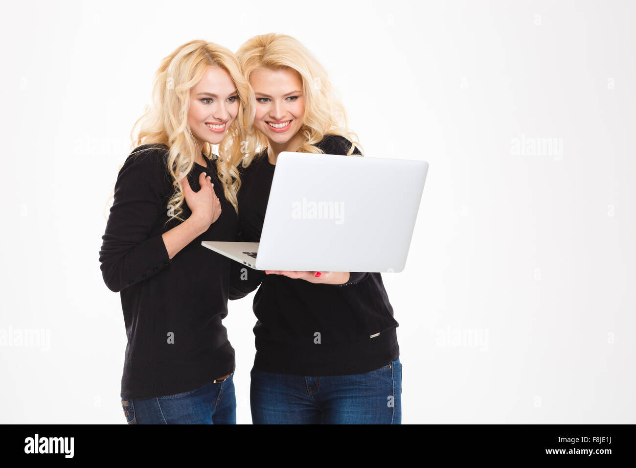 Portrait of a smiling sisters twins using laptop computer isolated on a ...