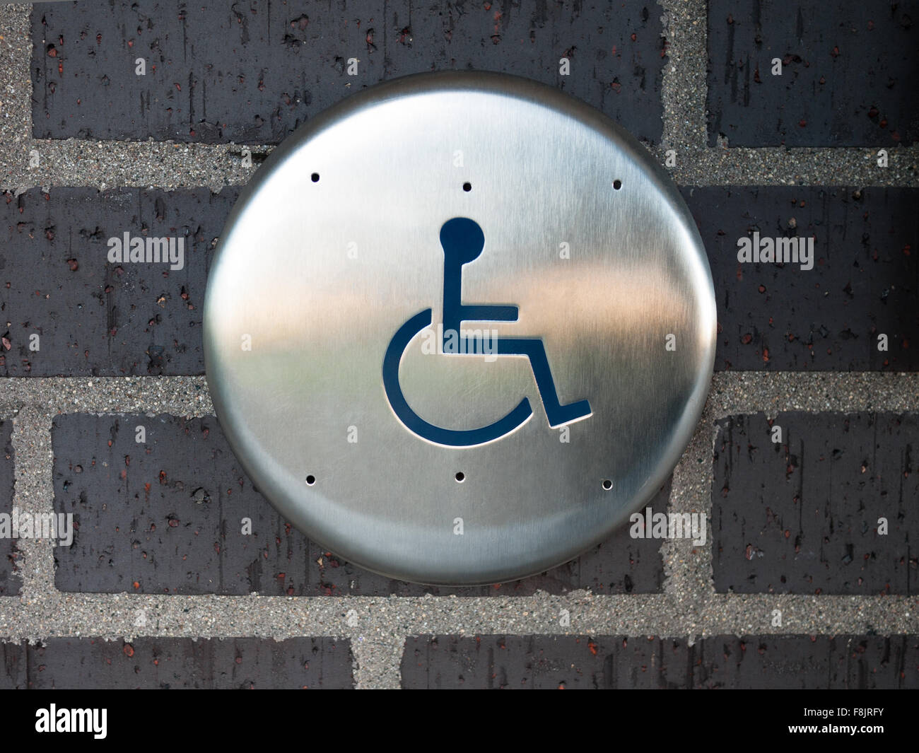 Handicapped disabled access automatic door opener button switch with a wheelchair symbol on a brick wall Stock Photo