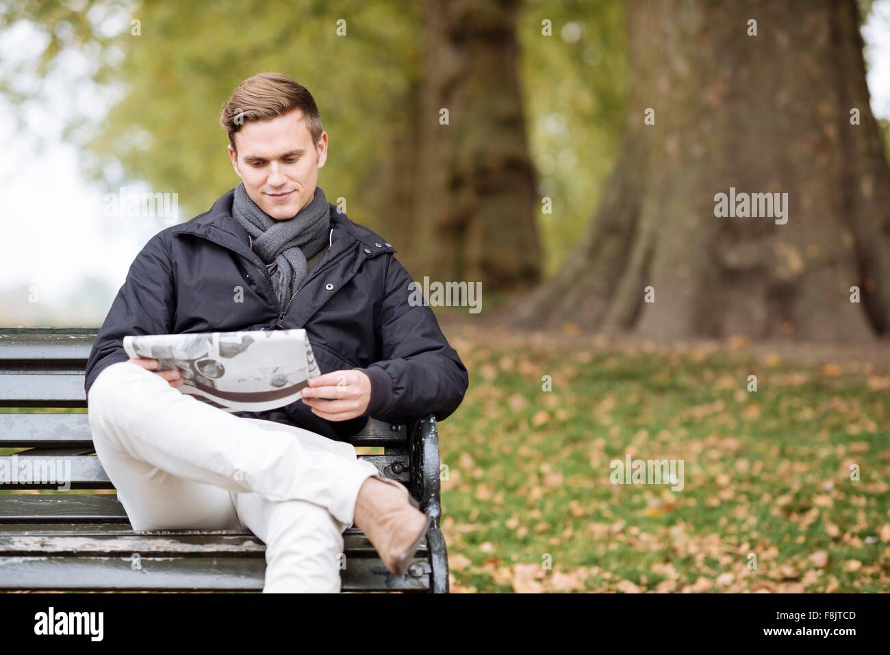 Young man reading newspaper on park bench Stock Photo - Alamy