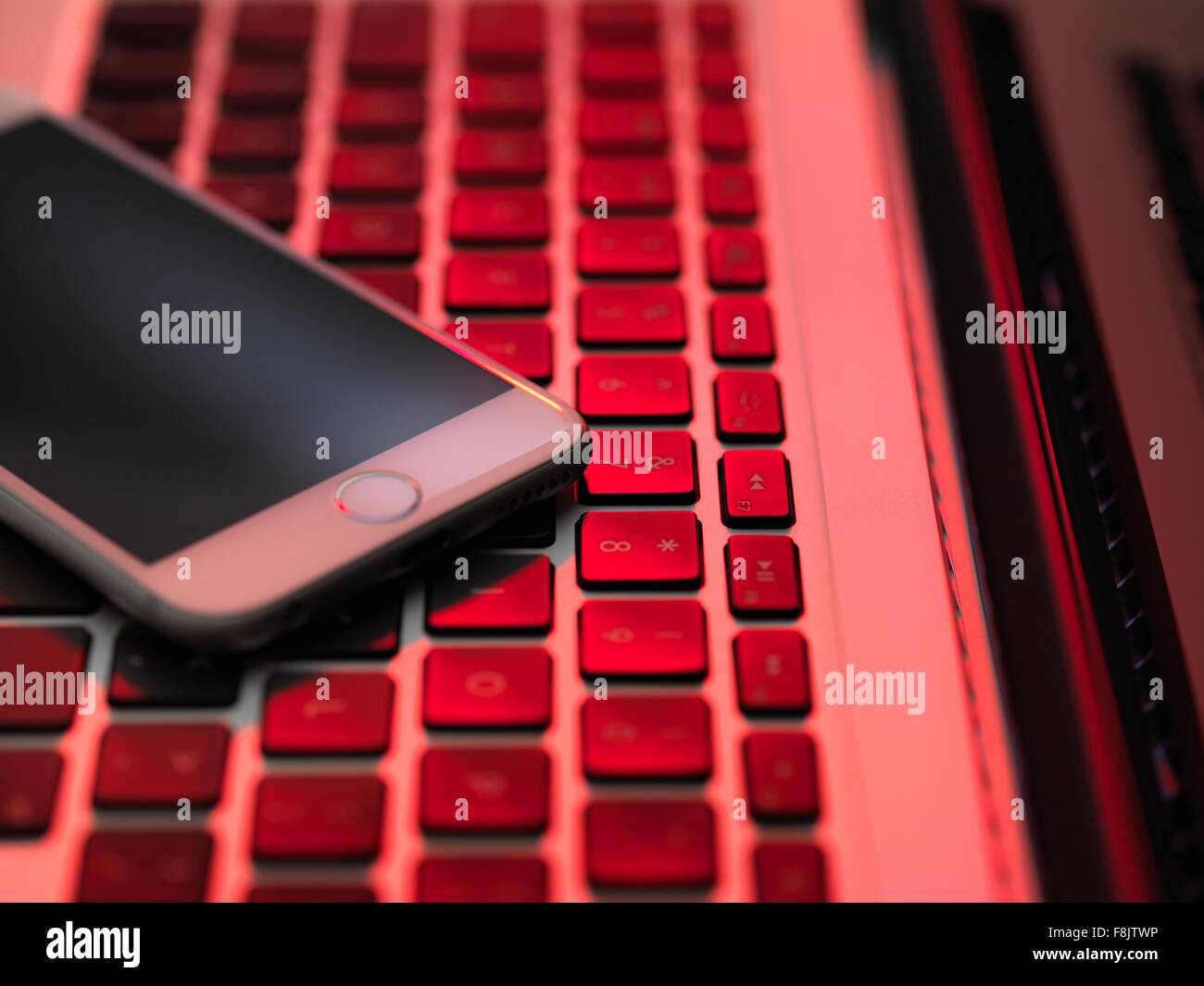 High angle view of cellular phone on computer keyboard in red lighting Stock Photo