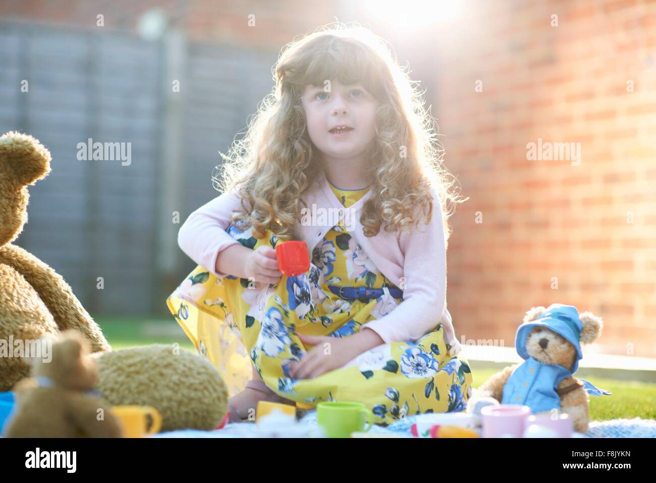 Girl having teddy bear picnic in garden holding toy teacup Stock Photo