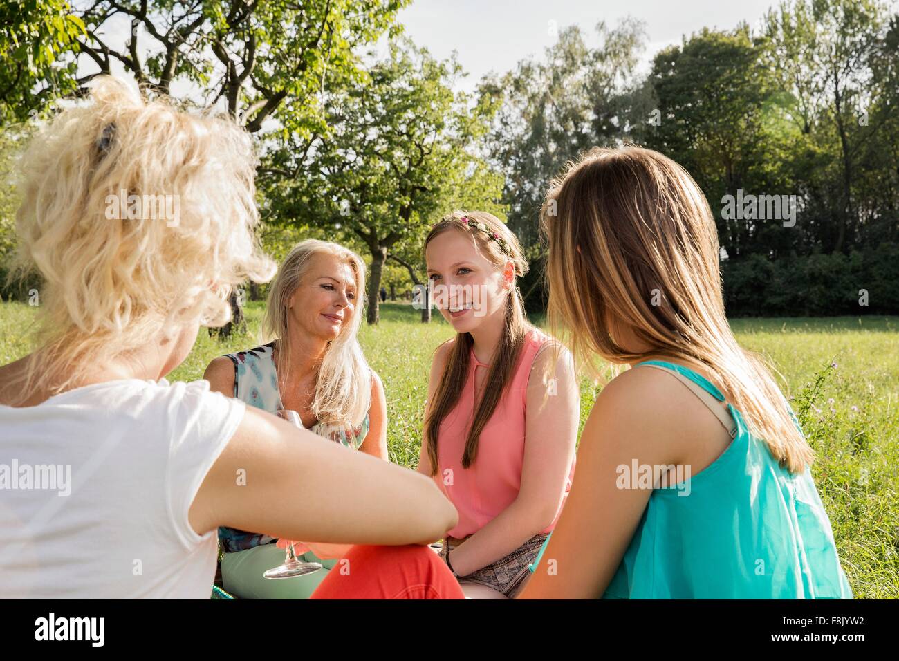 Women sitting in park drinking wine, talking and smiling Stock Photo