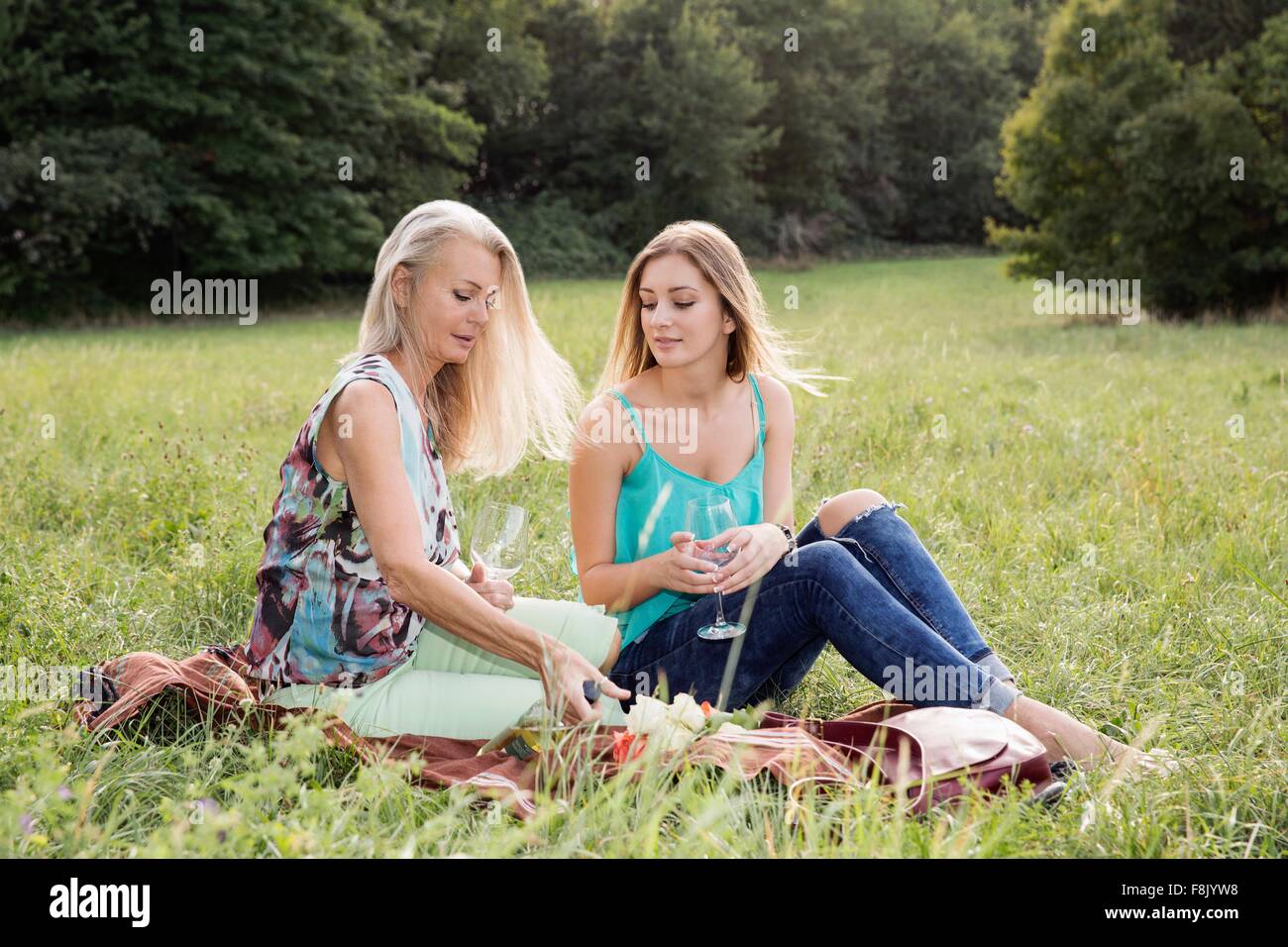Women sitting on picnic blanket in park enjoying a glass of wine Stock Photo