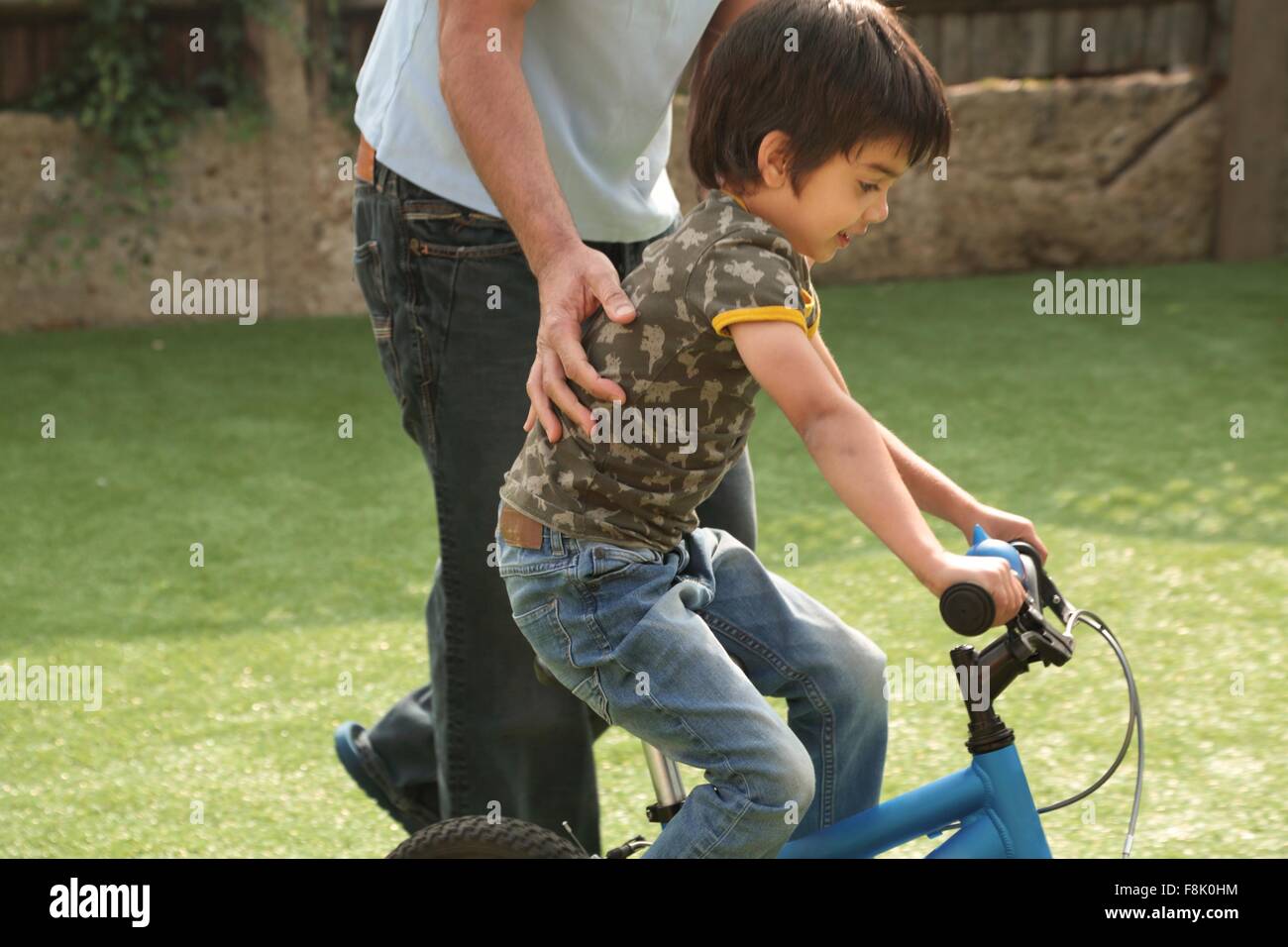 Side view of father supporting boy learning to ride bicycle Stock Photo