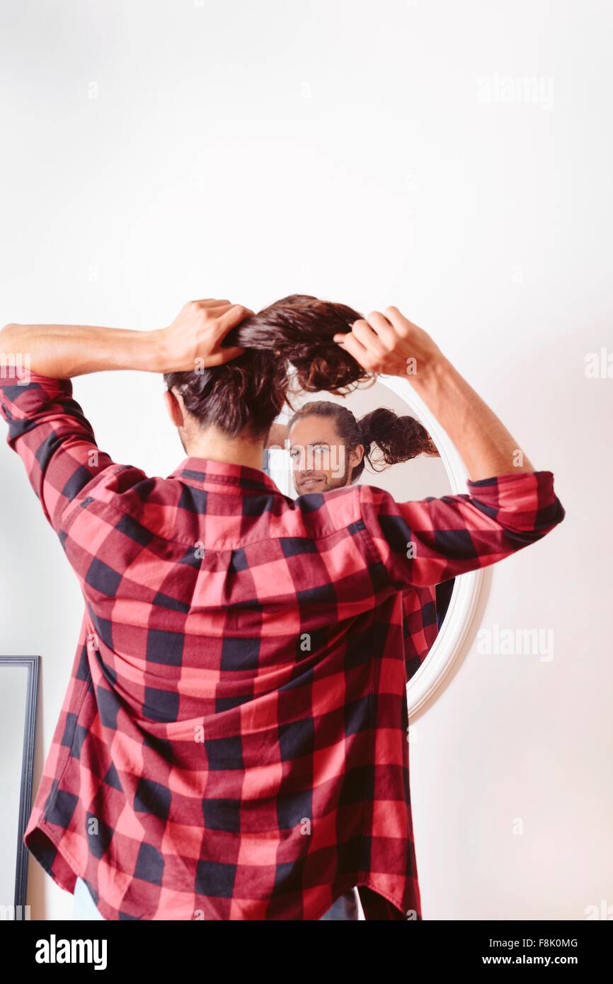 Young man looking in mirror, putting hair in ponytail, rear view Stock Photo
