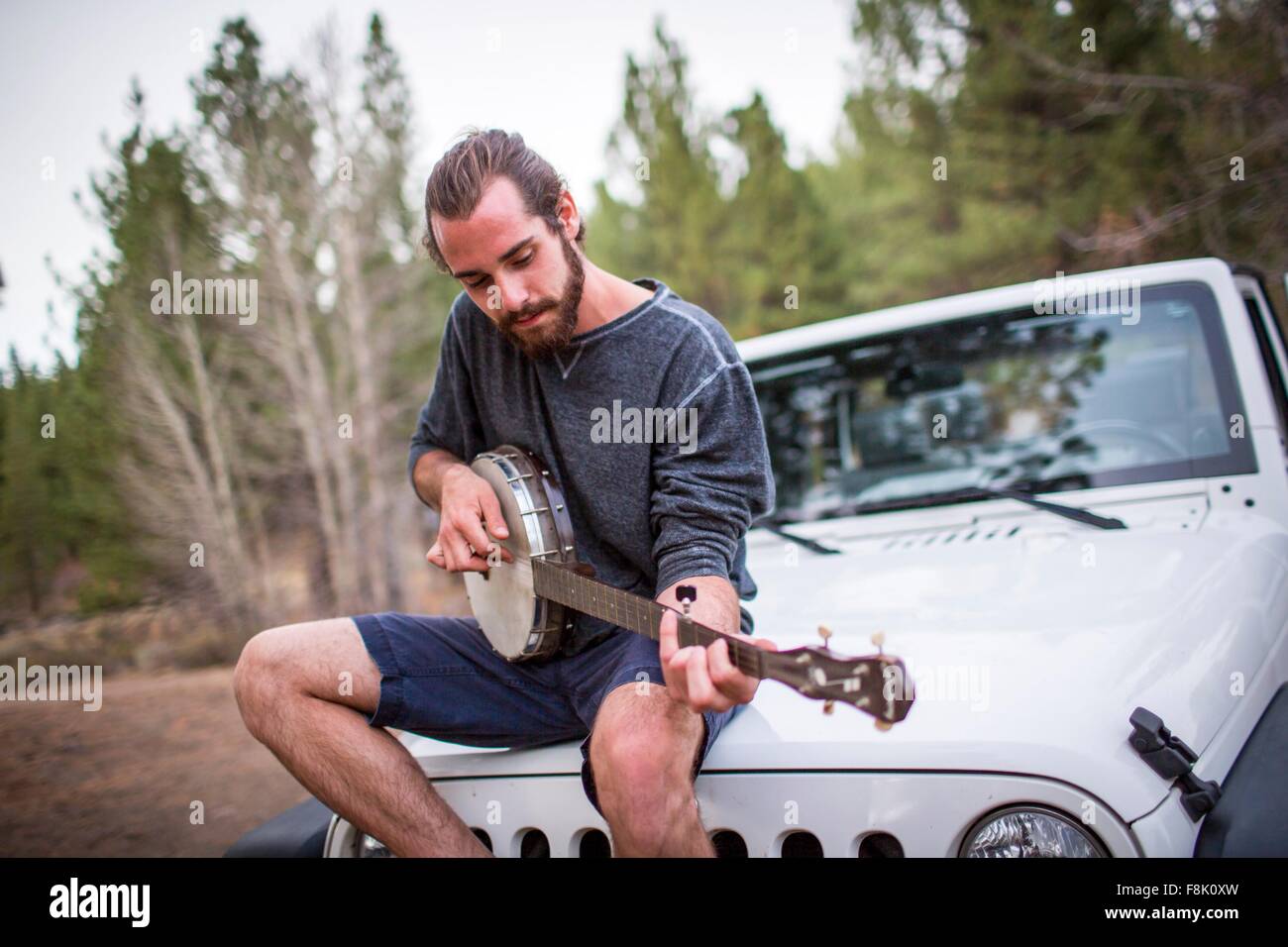 Young man playing banjo on jeep hood, Lake Tahoe, Nevada, USA Stock Photo