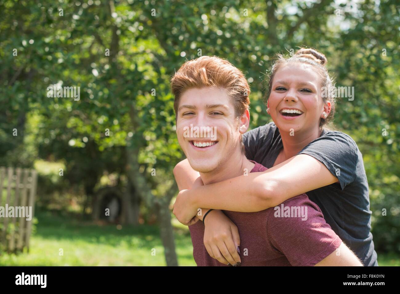 Portrait of young man giving young woman piggy back looking at camera smiling Stock Photo