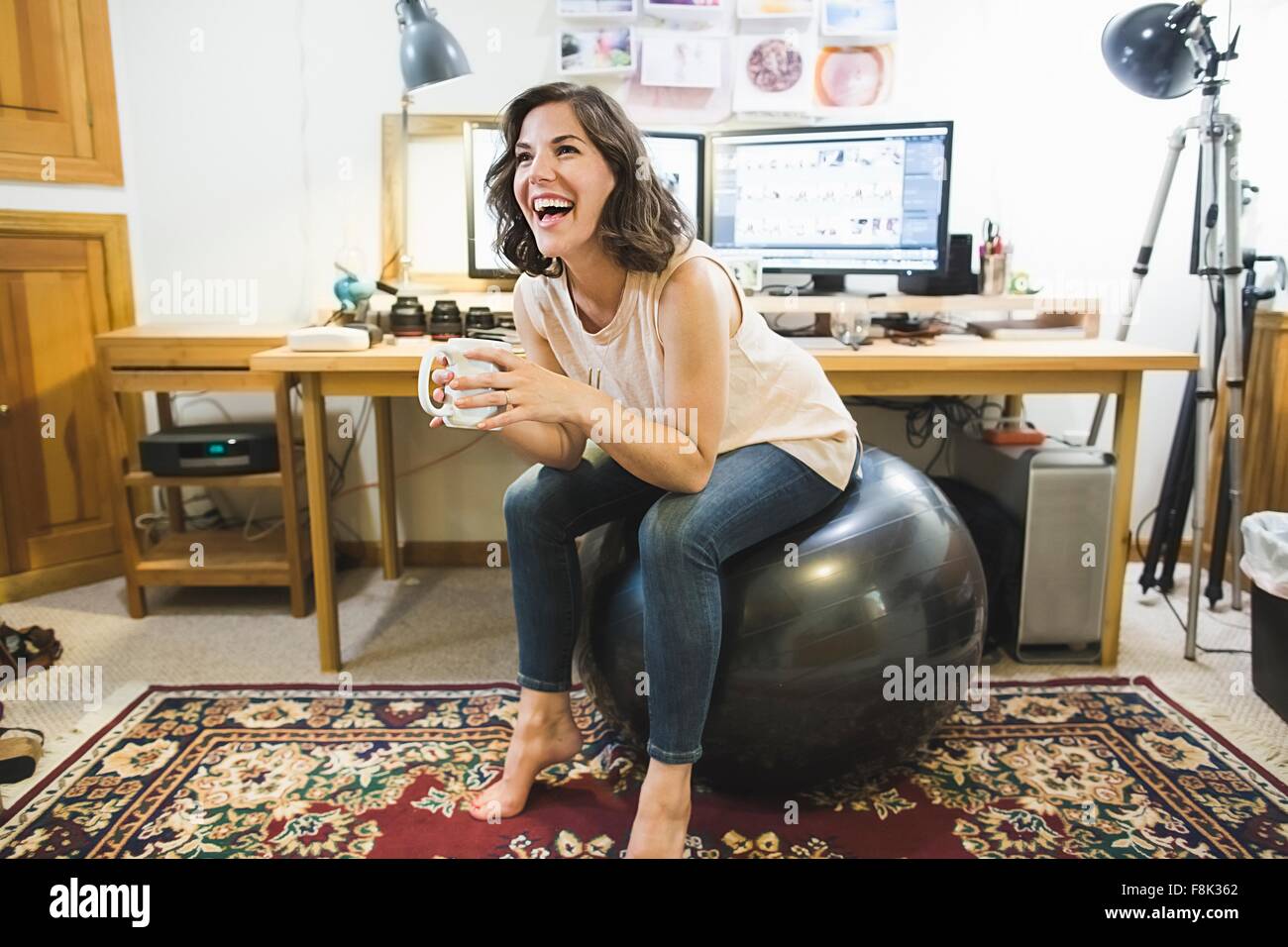 Mid adult woman sitting on yoga ball, holding coffee cup Stock Photo