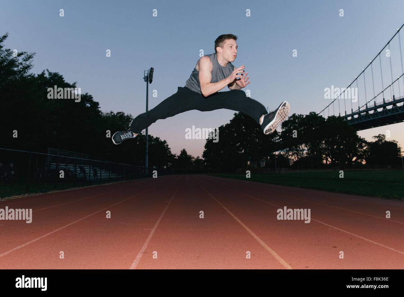 Young man jumping, mid air, on race track, sunset, low angle view Stock Photo