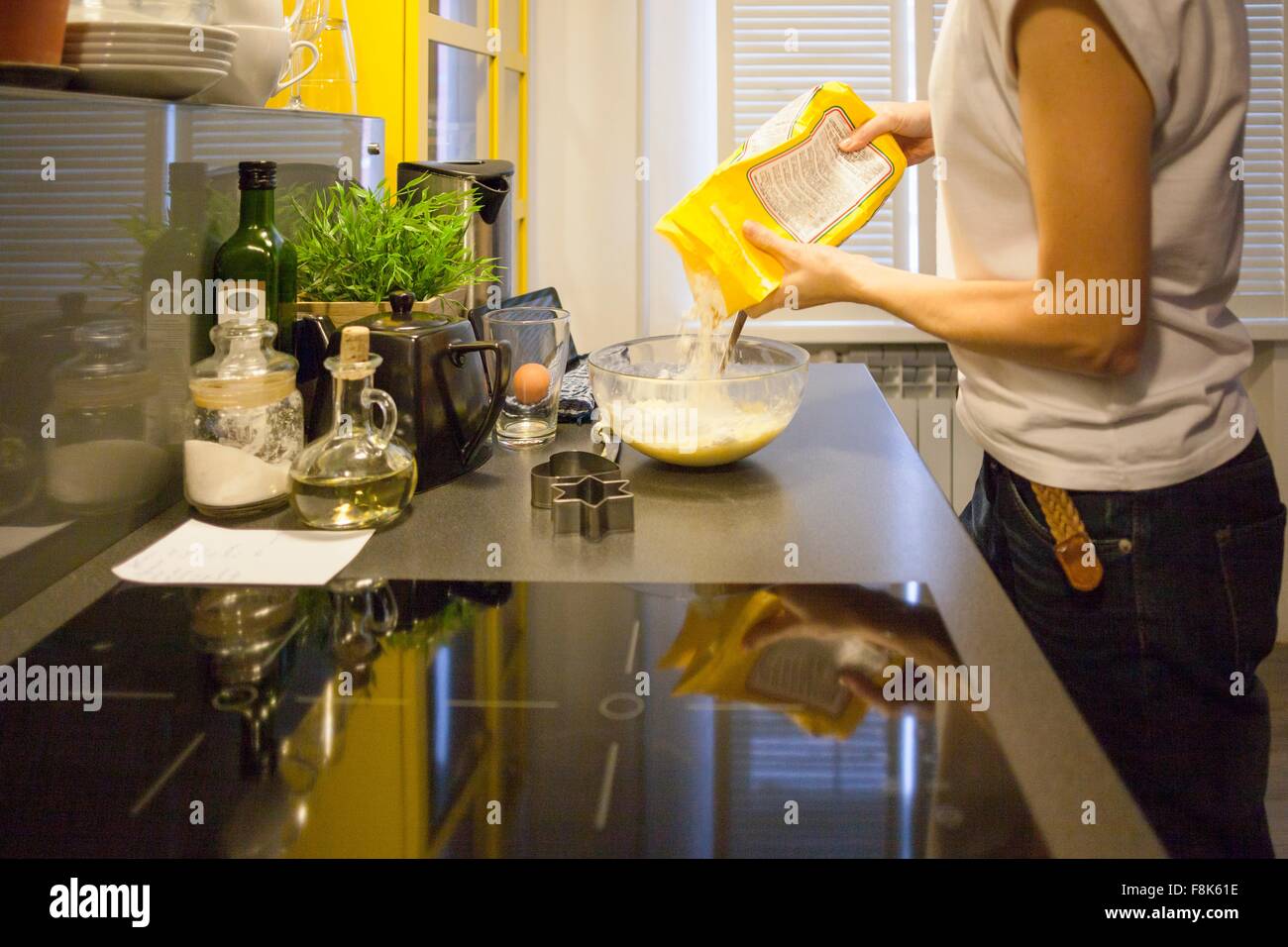 Mid adult woman pouring flour into mixing bowl at kitchen counter Stock Photo